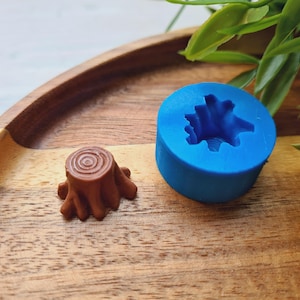 May include: A blue silicone mold shaped like a tree stump, and a brown resin tree stump on a wooden surface.