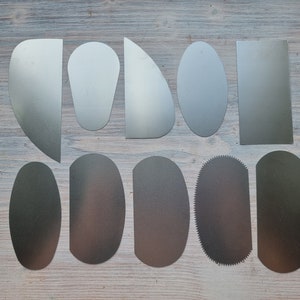 May include: Set of 10 metal sculpting tools with various shapes and sizes, including a rectangular tool, a rounded tool with a serrated edge, and several oval-shaped tools.