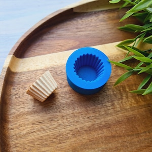 Op de afbeelding: Een blauwe siliconen cupcakevorm en een bruine papieren cupcakevorm op een houten oppervlak.