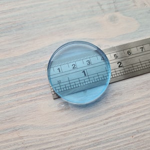 May include: A clear blue round disc measuring 1 1/2 inches in diameter, placed on top of a ruler.