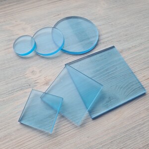 May include: A set of five clear blue acrylic sheets in various sizes and shapes, including circles and squares. The sheets are arranged on a light wood surface.