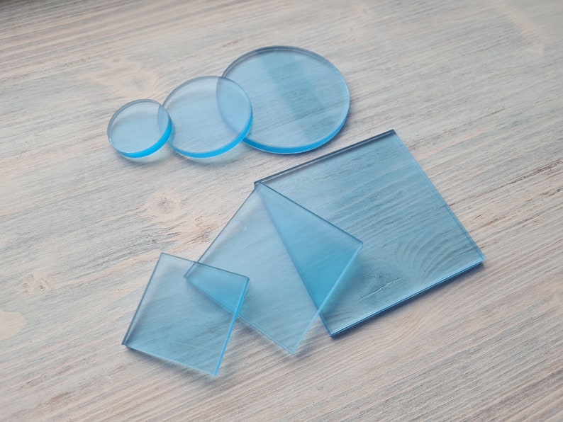 May include: A set of five clear blue acrylic sheets in various sizes and shapes, including circles and squares. The sheets are arranged on a light wood surface.