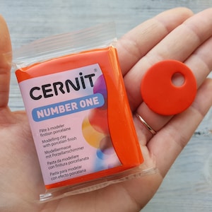 May include: A package of orange modeling clay with the brand name "CERNIT" and the text "NUMBER ONE". The package is labeled with the text "Pâte à modeler finition porcelaine" and "Modelling clay with porcelain finish".