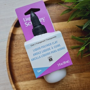 May include: A clear bottle of liquid polymer clay with a black cap. The bottle is labeled "Liquid Polymer Clay" in English, French, and Spanish. The bottle is 2 fl oz (59 mL).