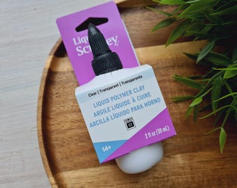 May include: A clear bottle of liquid polymer clay with a black cap. The bottle is labeled "Liquid Polymer Clay" in English, French, and Spanish. The bottle is 2 fl oz (59 mL).