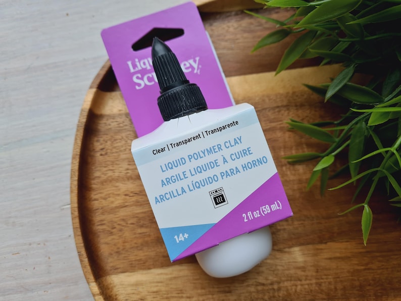 May include: A clear bottle of liquid polymer clay with a black cap. The bottle is labeled "Liquid Polymer Clay" in English, French, and Spanish. The bottle is 2 fl oz (59 mL).