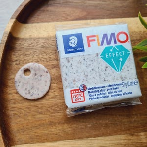 May include: A package of FIMO Effect modeling clay, a white and gray speckled clay with a diamond-shaped logo. The package includes instructions for baking the clay at 110°C (230°F).