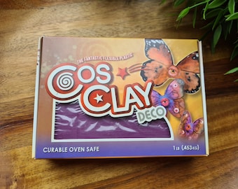 Può includere: Una scatola di Cos Clay Deco, una plastica curabile in forno. La scatola presenta un blocco di argilla viola e illustrazioni di farfalle. Il testo sulla scatola recita "The Fantastic Flexible Plastic" e "1 lb (453 kg)".
