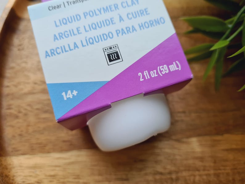 May include: A purple and blue box with the text "LIQUID POLYMER CLAY ARGILE LIQUIDE &Agrave; CUIRE ARCILLA L&Iacute;QUIDO PARA HORNO" and a picture of an oven. The box also says "14+" and "2 fl oz (59 mL)".