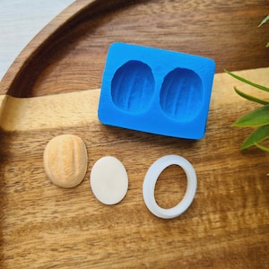 Könnte beinhalten: Eine blaue Silikonform mit zwei Hohlräumen in Walnussform. Auf einer Holzoberfläche liegen zwei weiße Kreise und ein braunes walnussförmiges Objekt.