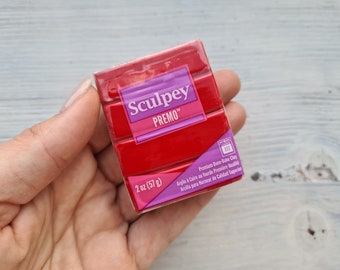 May include: A 2 ounce (57 gram) package of red Sculpey Premo oven-bake clay. The package is labeled with the brand name, product name, weight, and instructions for baking the clay.