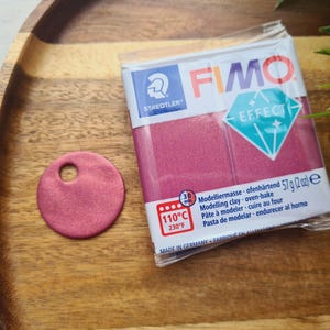 May include: A package of pink FIMO Effect modeling clay next to a small, round, pink clay piece with a hole. The package has the text "FIMO EFFECT" and "oven-bake" instructions. The clay is 57g (2 oz).