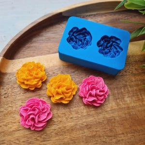 Puede incluir: Cuatro moldes de silicona para hacer decoraciones con forma de flor. Los moldes son azules y tienen dos formas de flor cada uno. También hay cuatro decoraciones de flores terminadas en rosa y amarillo.