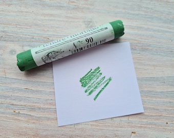 May include: A green pastel stick with the text "tendre - morbido" and "N° 90" on the label. A green mark is drawn on a white paper.