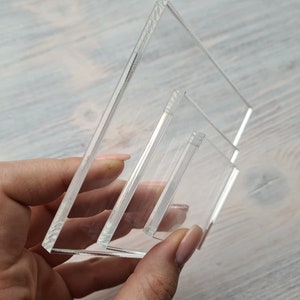 May include: A set of three clear acrylic display stands, stacked on top of each other. The stands are rectangular and have a slight bevel on the edges.