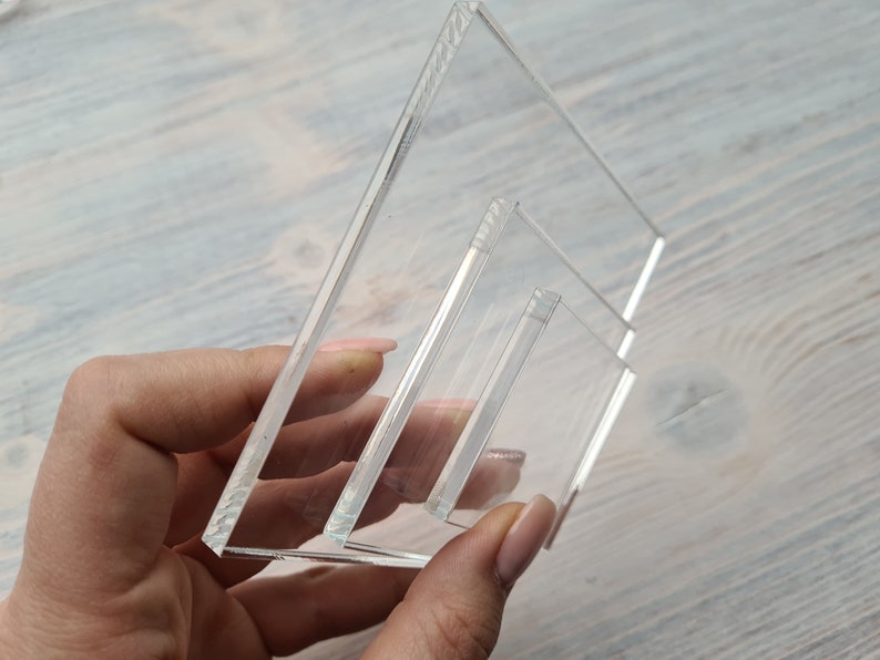 May include: A set of three clear acrylic display stands, stacked on top of each other. The stands are rectangular and have a slight bevel on the edges.