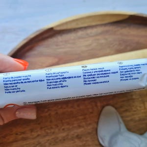 Pode incluir: Close-up de um tubo branco com texto azul descrevendo os usos do produto em v&aacute;rios idiomas. O texto inclui "Pasta de papier mache", "Pasta di cartapesta", "Паста папье-маше" e "&Chi;&alpha;&rho;&tau;&omicron;&pi;&omicron;&lambda;&tau;&omicron;&sigmaf; &alpha;&pi;&epsilon;&lambda;&epsilon;".
