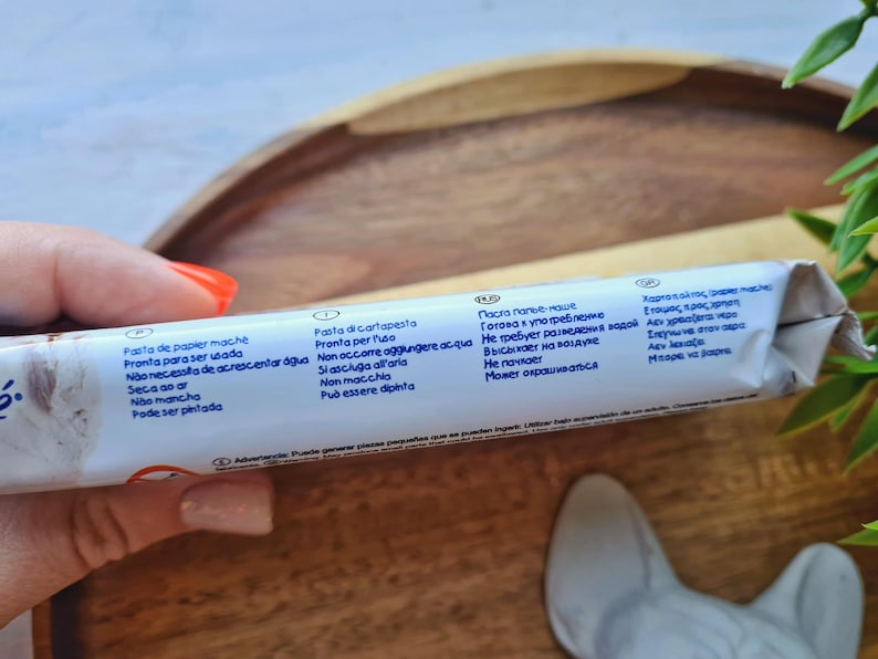 Pode incluir: Close-up de um tubo branco com texto azul descrevendo os usos do produto em v&aacute;rios idiomas. O texto inclui "Pasta de papier mache", "Pasta di cartapesta", "Паста папье-маше" e "&Chi;&alpha;&rho;&tau;&omicron;&pi;&omicron;&lambda;&tau;&omicron;&sigmaf; &alpha;&pi;&epsilon;&lambda;&epsilon;".