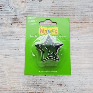 May include: A green package with the text "Makin's Cutter Set - Quality" and "Qualité supérieure" on it. The package contains three black metal star-shaped cookie cutters.