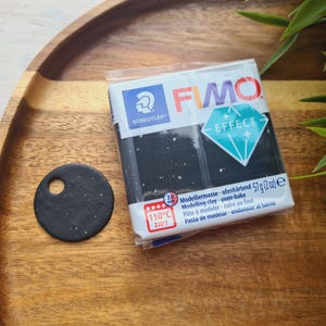 May include: A package of black FIMO Effect modeling clay with a white label. The label has the FIMO logo and the text "Modelliermasse ofenhärtend 57g (2oz) e Modelling clay oven-bake Pâte à modeler cuire au four Pasta de modelar endurecer al horno 110°C 230°F".