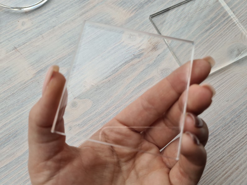 May include: A clear glass square, held in a hand, with a smooth surface.