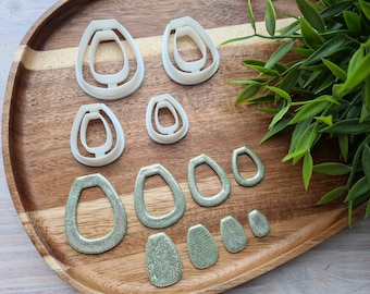 May include: A set of eight white plastic earring molds in various sizes, arranged on a wooden tray.  Next to the molds are eight green resin earrings, also in various sizes.