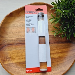 May include: A clear acrylic clay roller by Sculpey packaged on a rectangular cardboard backing. The packaging features the brand name Sculpey, the product name Acrylic Clay Roller in multiple languages, and a small graphic showing the tool in use.