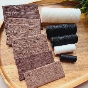 Könnte beinhalten: Ein Holztablett enthält braune, holzmasertexturierte Rechtecke und Spulen mit weißem und schwarzem Faden. Die Rechtecke variieren in ihren Brauntönen. Die Fadenrollen sind zylindrisch.