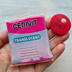 May include: A pink package of translucent polymer clay by Cernit. The package has the brand name Cernit and the word Translucent printed on it. The package also has text in multiple languages describing the product. A small pink circle with the number 474 written on it is visible in the background.