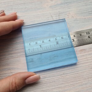 May include: A clear blue glass square with a ruler measuring 7 inches in length. The ruler is marked in inches and 1/16ths of an inch.