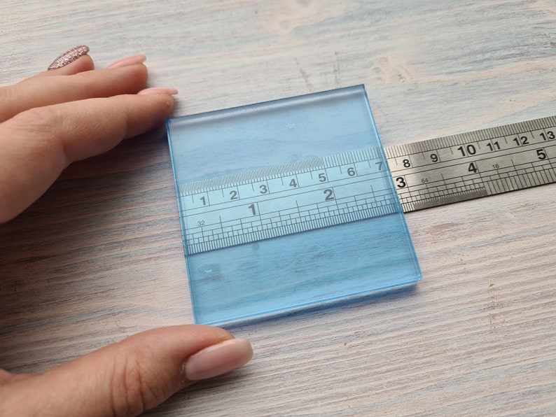 May include: A clear blue glass square with a ruler measuring 7 inches in length. The ruler is marked in inches and 1/16ths of an inch.