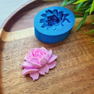 May include: A blue silicone mould shaped like a flower, and a pink sugar flower on a wooden surface.