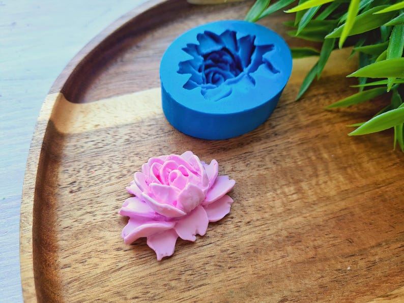 May include: A blue silicone mould shaped like a flower, and a pink sugar flower on a wooden surface.