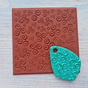 May include: A red rubber stamp with a pattern of circles, and a teal-colored silicone mold with the same pattern.