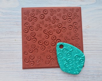 Pode incluir: Um carimbo de borracha vermelho com um padrão de círculos e um molde de silicone turquesa com o mesmo padrão.