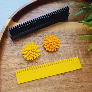 May include: Two yellow flower-shaped hair clips and a yellow plastic comb with a black plastic comb on a wooden surface.