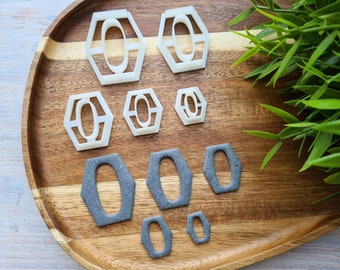 May include: A set of six cookie cutters in two different sizes. The larger cutters are white and shaped like a hexagon with a rounded oval inside. The smaller cutters are gray and have a similar shape, but are slightly smaller.