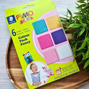 May include: A box of FIMO Kids Fancy Colour Pack modelling clay. The box features a colourful illustration of an owl and a girl holding a unicorn. The box contains six 42-gram bars of clay in the colours teal, gold, purple, pink, light pink, and white.