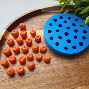 Puede incluir: Un molde de silicona azul con 36 cavidades redondas y 25 réplicas de fruta en miniatura de color naranja sobre una superficie de madera.