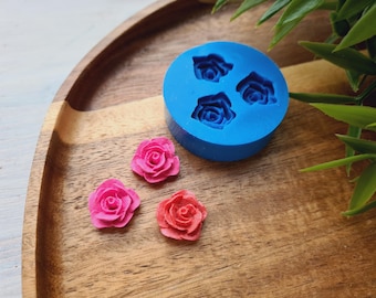 May include: A blue silicone mold with three rose-shaped cavities. Three pink resin roses are shown next to the mold.