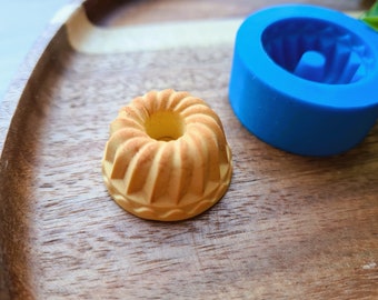 May include: A small, yellow cake mold made of silicone. The mold is shaped like a bundt cake and has a swirl design. The mold is sitting on a wooden surface.