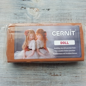 May include: A block of brown polymer clay in a clear plastic bag. The bag has a label that says "CERNIT DOLL" and "Modeling clay with porcelain finish".