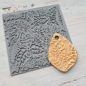 Peut inclure: Un moule en silicone gris avec un motif de feuilles détaillé et un pendentif en pâte polymère de couleur or avec un motif de feuilles assorti.