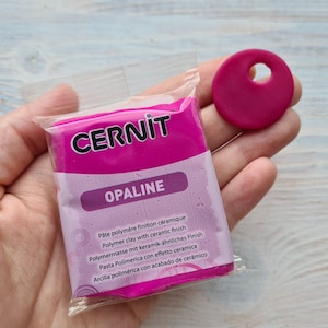 Może przedstawiać: Różowe opakowanie gliny polimerowej CERNIT OPALINE z ceramicznym wykończeniem. Opakowanie jest oznaczone nazwą marki i nazwą produktu białym tekstem. Opakowanie jest również oznaczone opisem produktu w wielu językach.