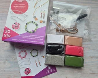 May include: A craft kit with 30 pieces for making jewelry. The kit includes colorful polymer clay, beads, tools, and instructions.  The box is purple and pink with the text "Makes 6 accessories! Fabriquez 6 accessoires! ¡Haz 6 accesories!" and "30 pc/pz".
