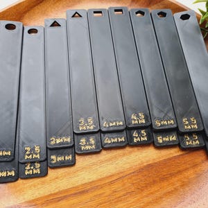 Peut inclure: Ensemble d'outils noirs et rectangulaires avec des formes vari&eacute;es en haut, comme un cercle, un triangle et un carr&eacute;. Chaque outil est &eacute;tiquet&eacute; avec du texte dor&eacute; indiquant des mesures de 2 mm &agrave; 6 mm.