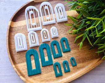 May include: A set of white and teal blue plastic cookie cutters shaped like arched windows. The cutters are arranged on a wooden surface.
