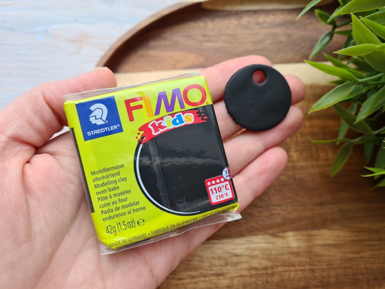 May include: A pack of black FIMO Kids modelling clay with the text "STAEDTLER FIMO kids" and "Modelliermasse ofenh&auml;rtend Modelling clay oven-bake P&acirc;te &agrave; modeler cuire au four Pasta de modelar endurence al horno 42g (1.5 oz) e MADE IN GERMANY FABRIQUE EN ALLEMAGNE 110&deg;C 230&deg;F". A black circle with a hole in the centre is in the background.