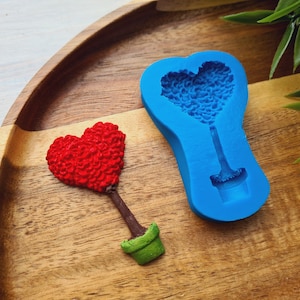 Op de afbeelding: Een rode hartvormige boom in een groene pot, naast een blauwe siliconen mal van hetzelfde ontwerp. De mal is voor het maken van hartvormige bomen.