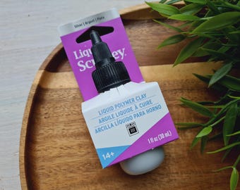May include: A bottle of Liquid Polymer Clay by Sculpey, a brand of polymer clay for crafting. The bottle is silver with a black cap and a purple label with white text. The label says "Liquid Polymer Clay", "Argile Liquide à Cuire", "Arcilla Líquido Para Horno", and "14+". The bottle is 1 fl oz (30 mL).
